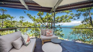 A balcony with a sofa and a small round table, overlooking a scenic view of the sea and trees. - Headland House (Picnic Bay)