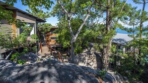 A modern building with a wooden deck, surrounded by trees and a rocky landscape. - Headland House (Picnic Bay)