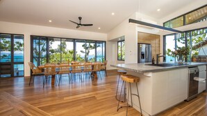 A spacious kitchen with a large island, modern appliances, and large windows offering views of the outdoors. - Headland House (Picnic Bay)
