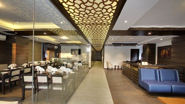 A modern hotel lobby with glass partitions, a reception desk, seating area, and a patterned ceiling. - Hotel Grandeur (Pune)