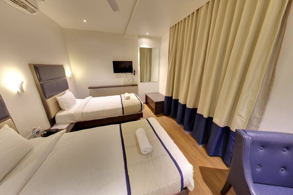 A hotel room with two beds, a TV, a mirror, and a window with curtains.