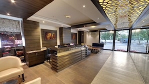 A modern hotel reception area with a wooden reception desk, seating, and artwork on the walls. - Hotel Grandeur (Pune)