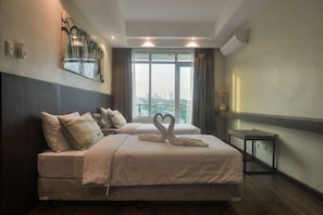 A hotel room with a large bed, a small bedside table, and a view of a cityscape through the window. - Comfy Suites at The Padgett Place (Cebu City)