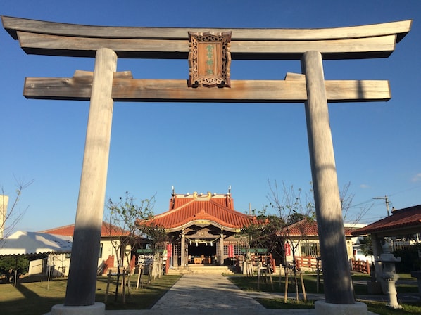 A traditional Japanese torii gate with a wooden frame and a decorative plaque, leading to a building with a red tiled roof and a covered entrance.