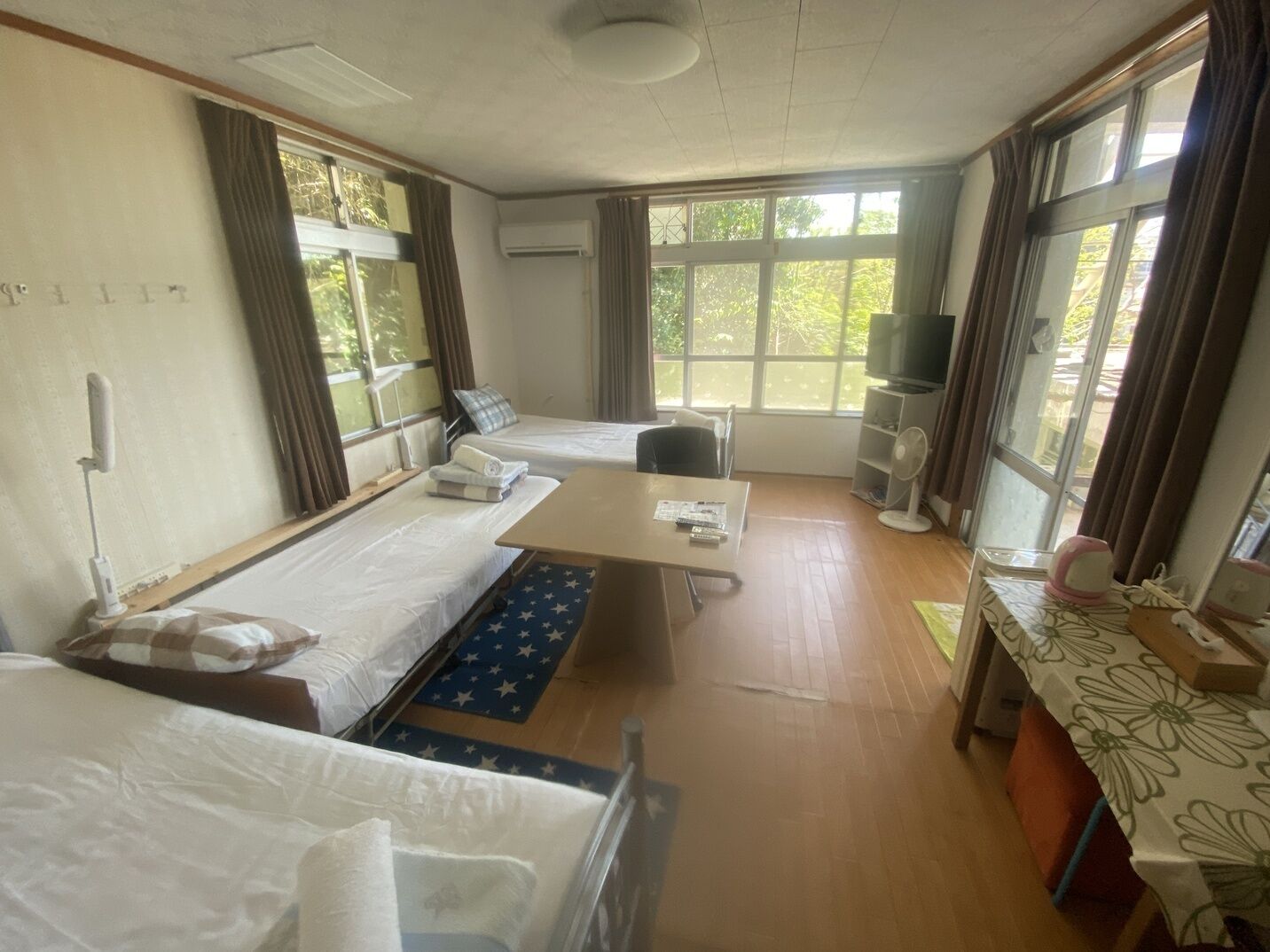 A hotel room with two beds, a desk, a chair, a TV, and large windows.