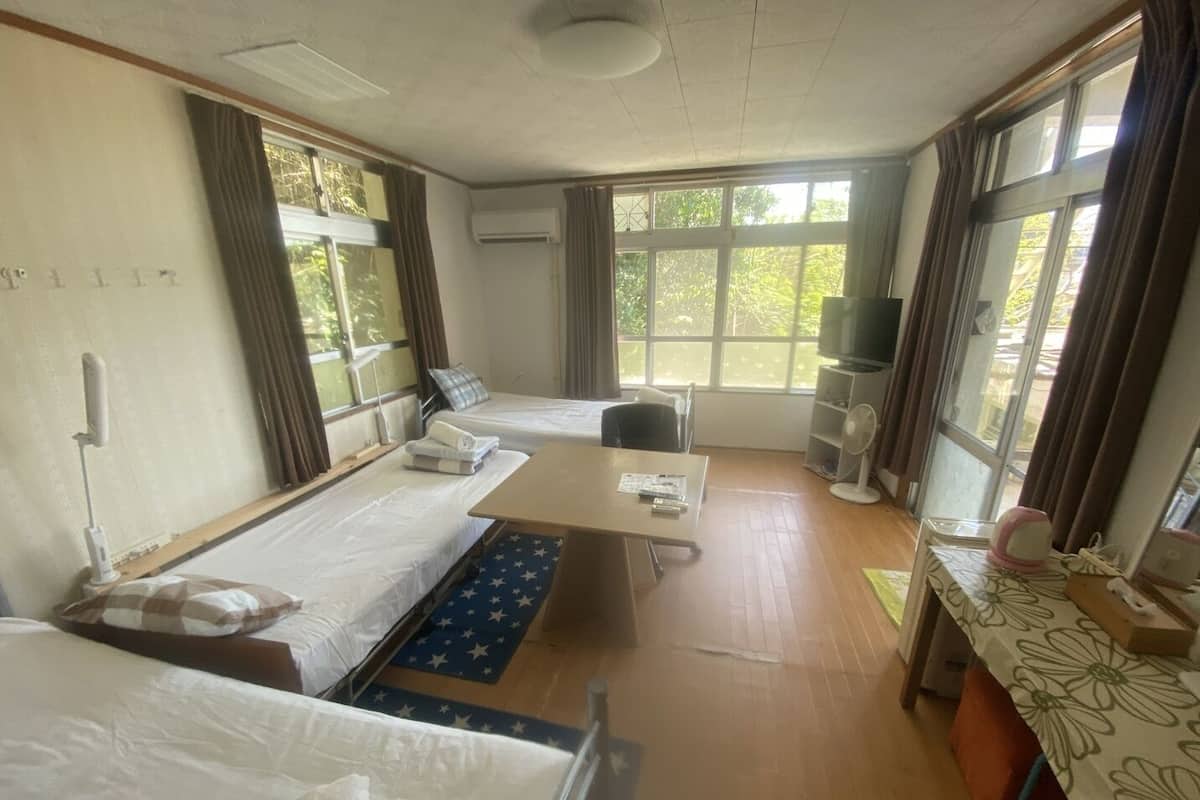 Een hotelkamer met twee bedden, een bureau, een stoel, een televisie en grote ramen.