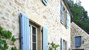 Ein Steinhaus mit blauen Fensterläden und einem Kopfsteinpflasterweg.