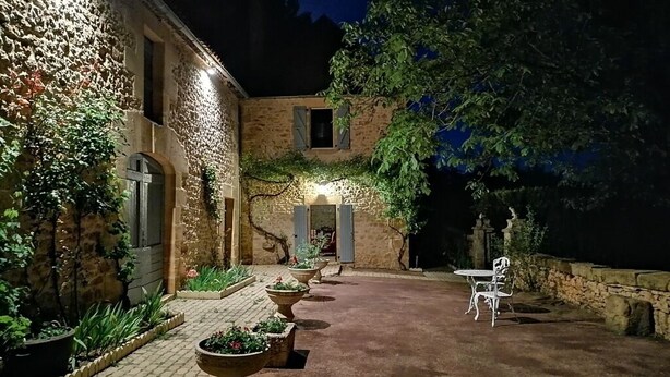 Ein Gebäude aus Stein mit einem gepflasterten Innenhof, Außenbestuhlung und Blumentöpfen.