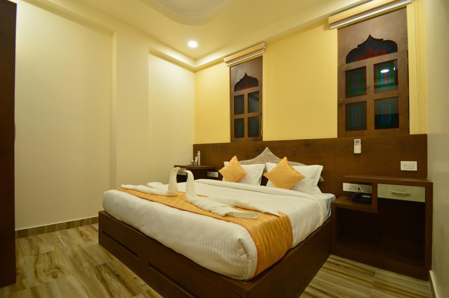A hotel room with a large bed, wooden headboard, bedside tables, and a small desk.