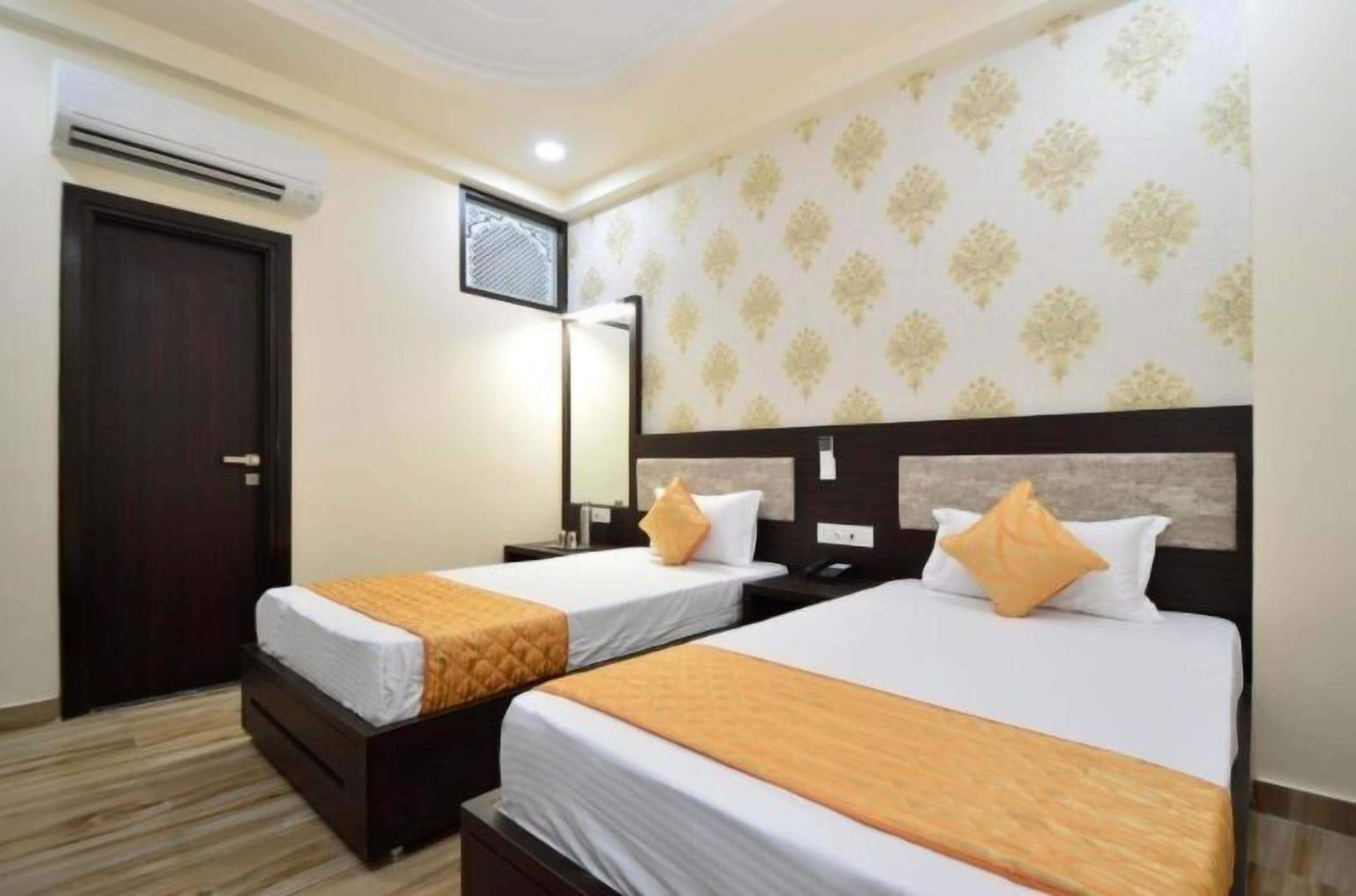 A hotel room with two beds, a dark wooden door, an air conditioning unit, a patterned wall, and a mirror.