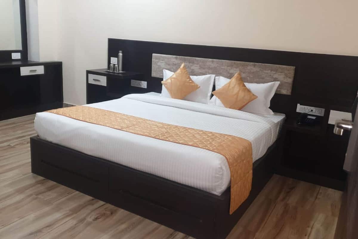 A hotel room with a large bed, a nightstand with a lamp, a dresser, and a mirror.