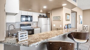 A modern kitchen with white cabinets, granite countertops, stainless steel appliances, and a bar area with wooden stools.
