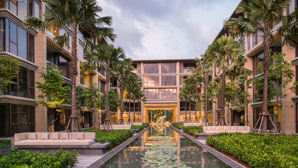 A modern hotel courtyard with a central reflective pool, palm trees, and a well-maintained garden. - Apartment on the Beach Maikhao Pool View 72sqm (Mai Khao)