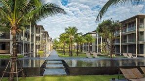 A modern hotel with a central water feature, palm trees, and outdoor seating areas. - Apartment on the Beach Maikhao Pool View 72sqm (Mai Khao)