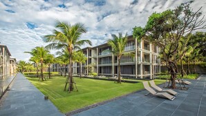 A modern hotel with a courtyard featuring palm trees, a swimming pool, and lounge chairs. - Apartment on the Beach Maikhao Pool View 72sqm (Mai Khao)