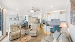 A spacious living area with a sofa, chairs, and a dining table. There is a kitchen area with cabinets and a refrigerator. - Sea Gull #808: Beachfront 2 Bedroom 2 Bath with Spectacular Views and 24 Hour Management (Port Aransas)