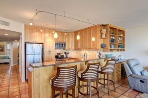 A kitchen with wooden cabinets, a stainless steel refrigerator, a bar area with stools, and pendant lighting.
