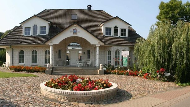 A two-story house with a tiled roof, a brick facade, and a central entrance with a small porch.