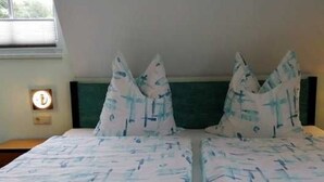 A bed with a white and blue patterned bedspread and matching pillows, a bedside table with a lamp, and a window with blinds.