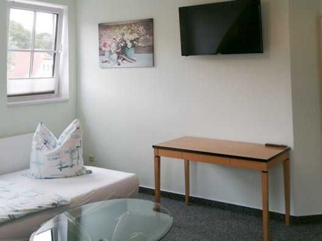A room with a bed, a small table, a television mounted on the wall, and a window.