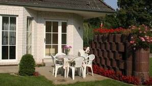 A house with a brick exterior, a covered patio with a table and chairs, and a brick wall with red flowers.