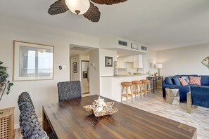 En moderne stue med et træspisebord, en blå sofa og et køkkenområde med hvide skabe og et rustfrit stål køleskab.