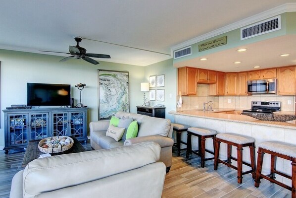 A modern living room with a sofa, TV, and a dining area with bar stools.