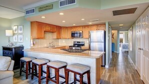 Una cocina con armarios de madera, una isla central con taburetes, un refrigerador y un microondas.