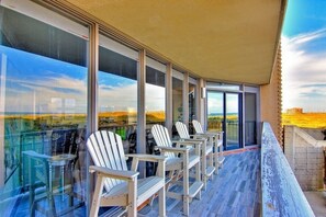 A balcony with white Adirondack chairs and a glass railing overlooking a scenic landscape.