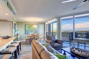 A spacious living room with a large window overlooking a scenic view, a dining area with a table and chairs, and a cozy seating area with a sofa and armchairs.