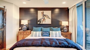 Un dormitorio con una cama grande, un ventilador de techo, un cuadro colgado en la pared de un pájaro y dos mesitas de noche con lámparas.