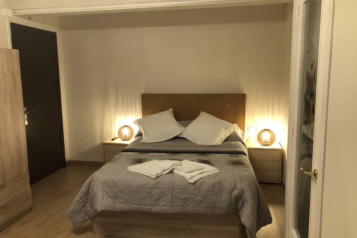 Quarto com cama, duas mesas de cabeceira, cabeceira de madeira e uma porta.