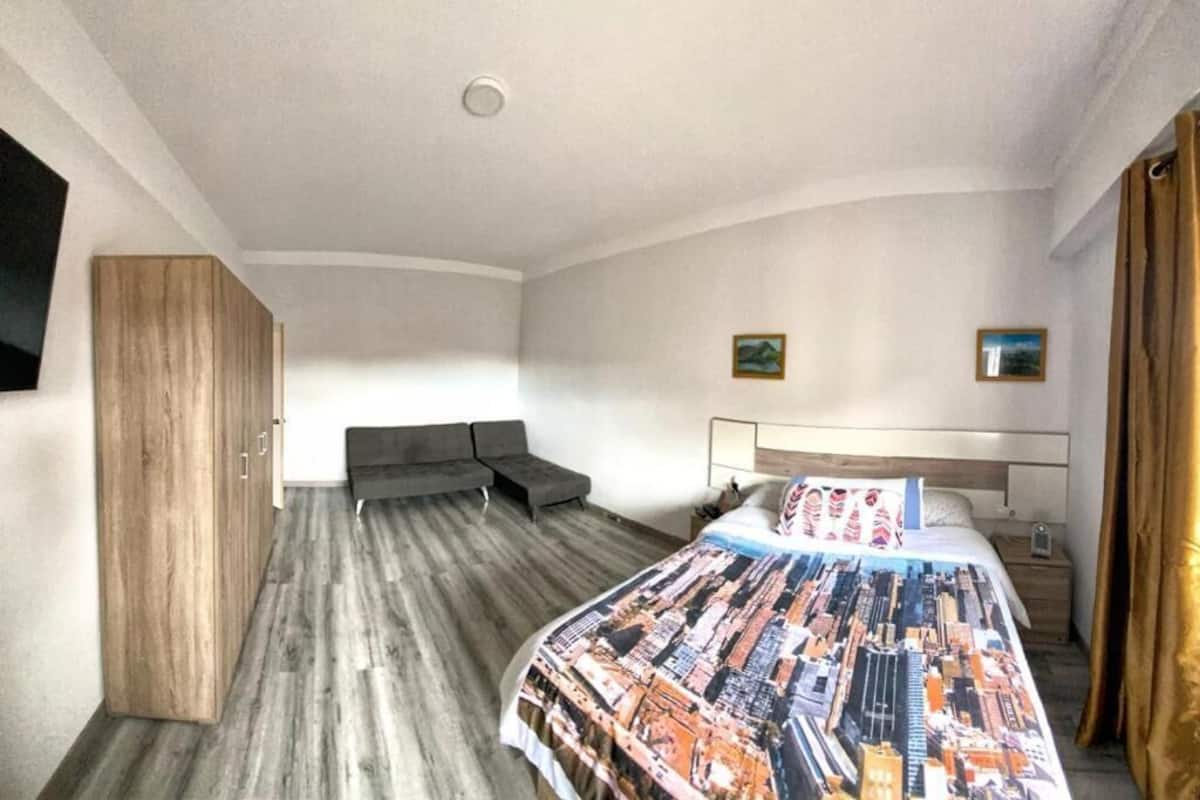 Quarto de hotel com cama, sofá, guarda-roupa e televisão.