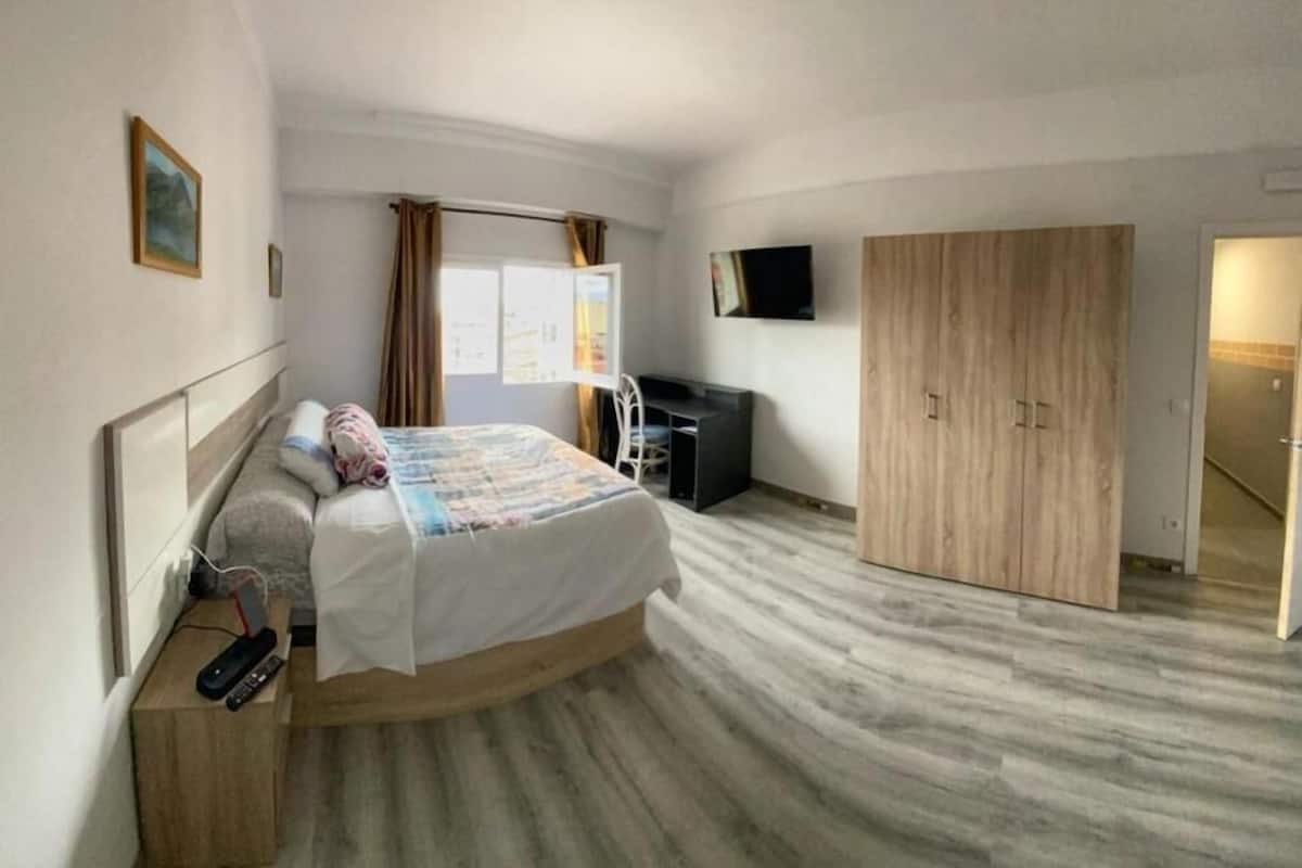 Quarto de hotel com uma cama, escrivaninha, televisão e armário.