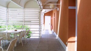 A covered outdoor seating area with tables and chairs, a tiled floor, and a corridor with a door and a sign.