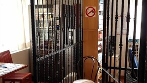 A room with a dining table and chairs, a chair with a woven seat, a tiled floor, and a barred door with a no-smoking sign.