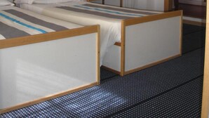 A room with two single beds, a ceiling fan, a painting, and a shower area.