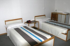 Una habitación con dos camas individuales, una mesita con un bolso rojo y un escritorio con una lámpara.