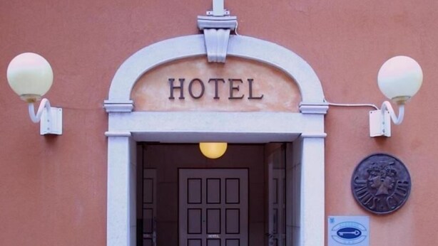 A hotel entrance with a sign above the door, a lamp post, and a plaque on the wall.