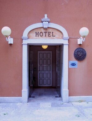 Entrada de un hotel con un letrero sobre la puerta, una farola y una placa en la pared.
