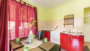Een kleine keuken met rode kastjes, een witte vaatwasser en een betegelde spatwand.
