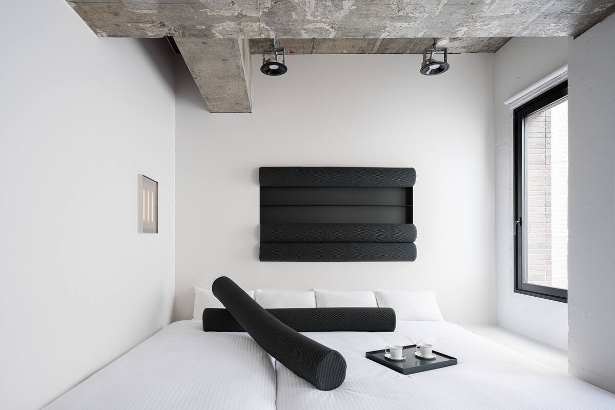 A modern bedroom with a large bed, a black headboard, and a window providing natural light.