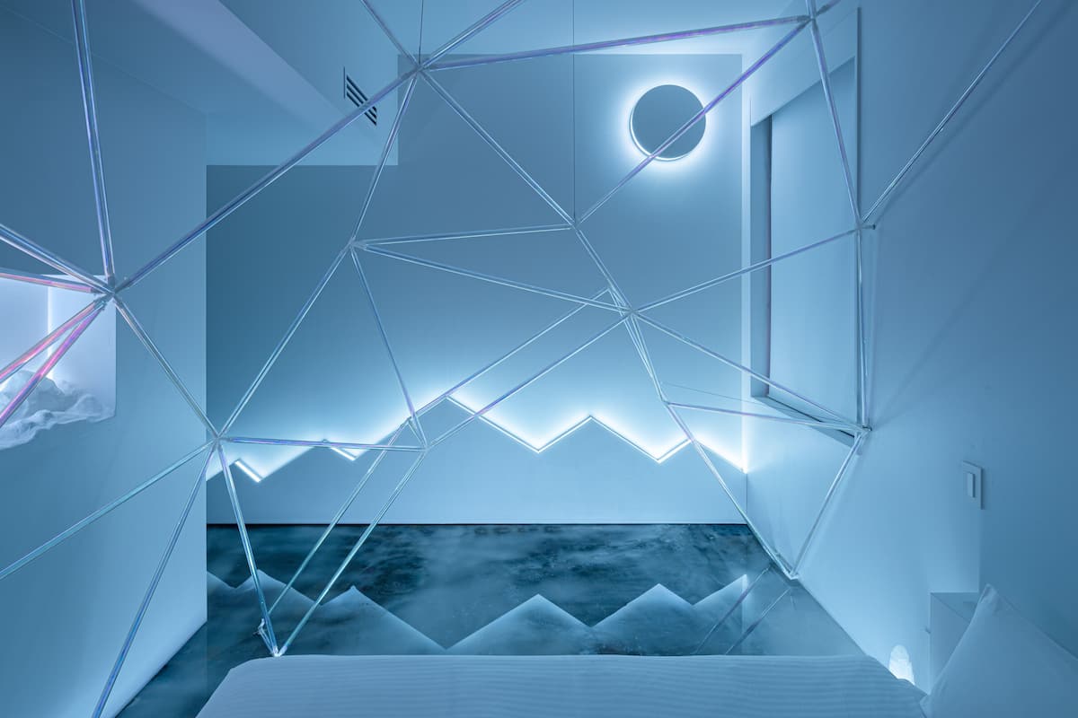 A modern hotel room with geometric ceiling design, a circular light fixture, and a view of the outdoors.