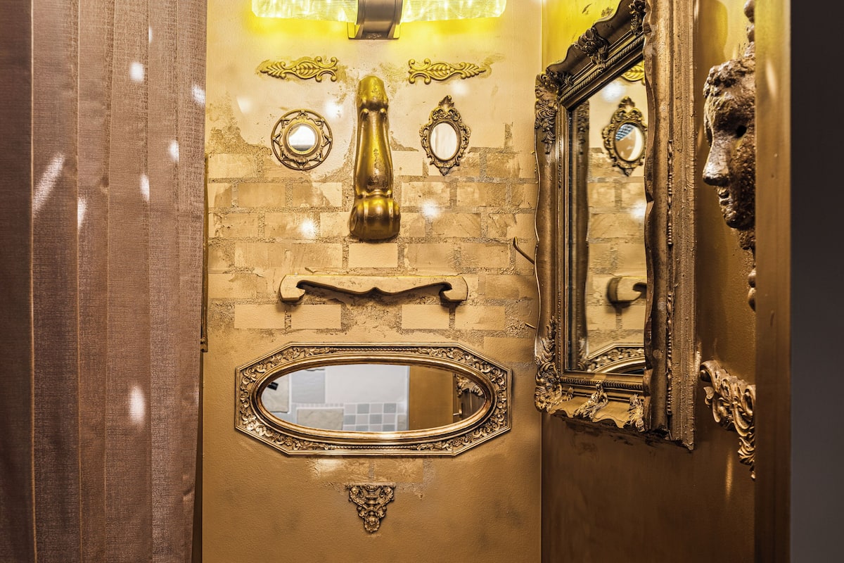 A bathroom with a gold vanity, a mirror, and a light fixture above the sink.