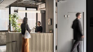 A reception area with a wooden counter, a potted plant, and a framed artwork on the wall. - BnA_WALL (Tokyo)