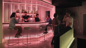 A modern bar area with a curved counter, bar stools, and a variety of bottles on shelves. - BnA_WALL (Tokyo)