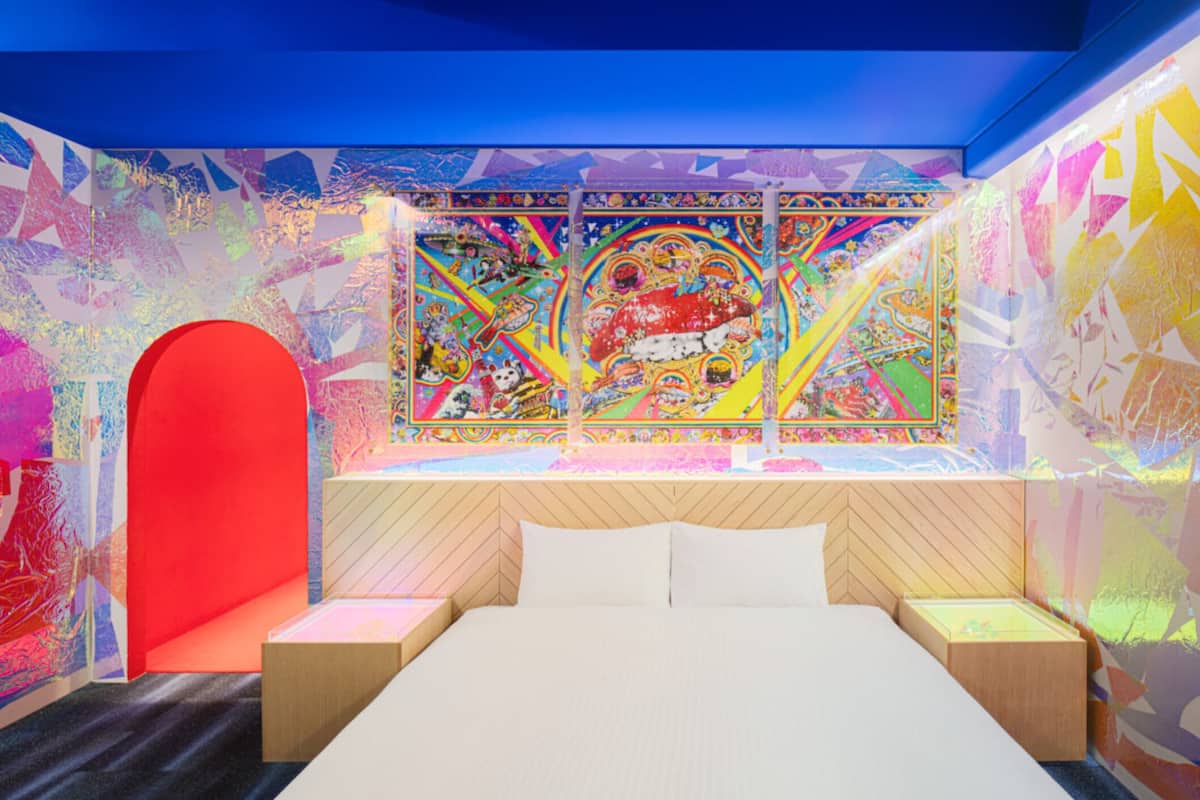 A modern hotel room with a large bed, a vibrant wall mural, and a unique red archway.