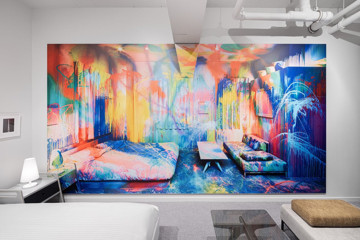 A modern hotel room with a large abstract painting on the wall, a bed, a desk, and a seating area.