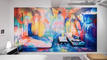 A modern hotel room with a large abstract painting on the wall, a bed, a desk, and a seating area.