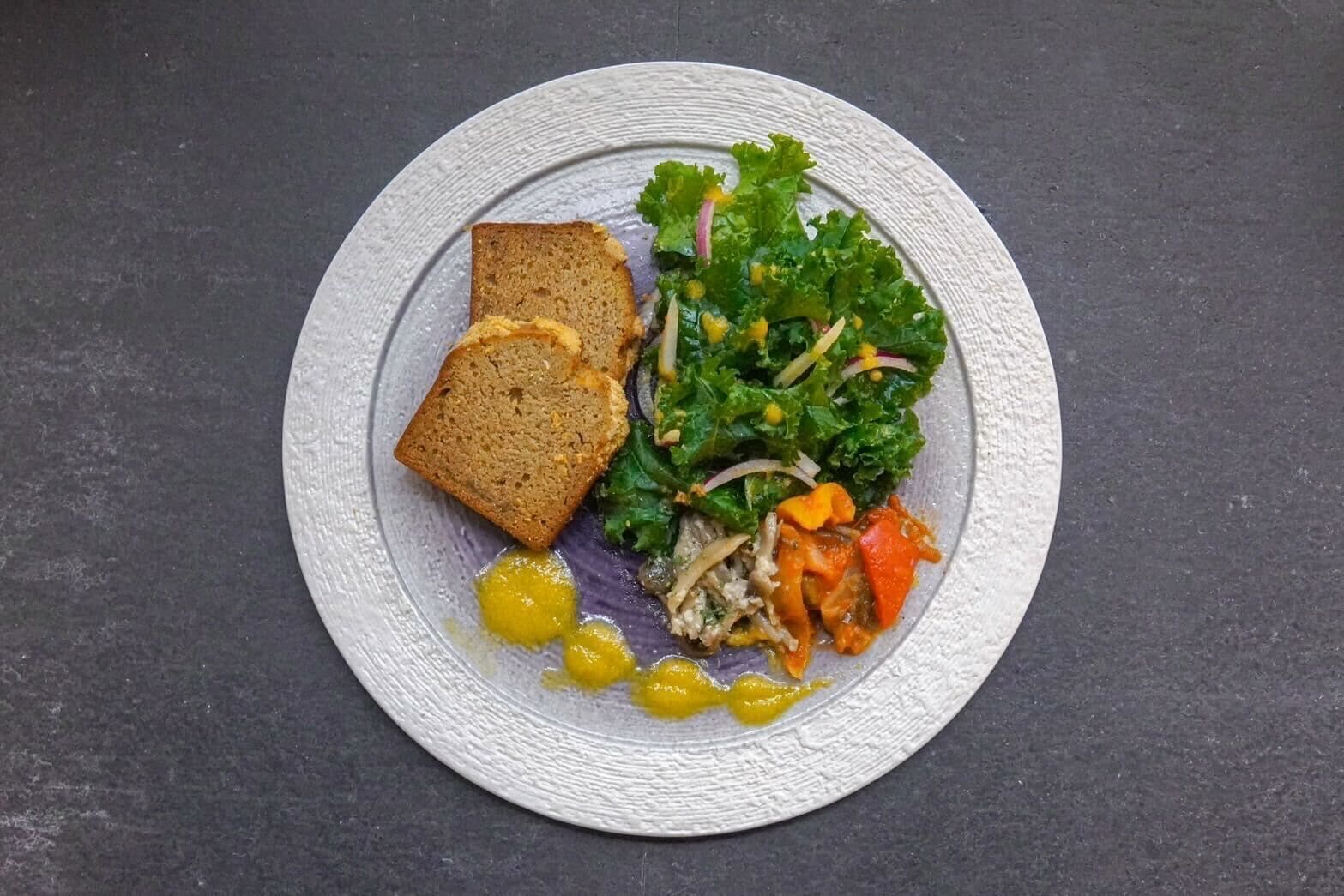 A plate with a slice of bread, a salad, and a small amount of mustard.